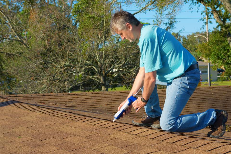 A roofing professional in a blue shirt applies a sealant to a red flat-top roof.